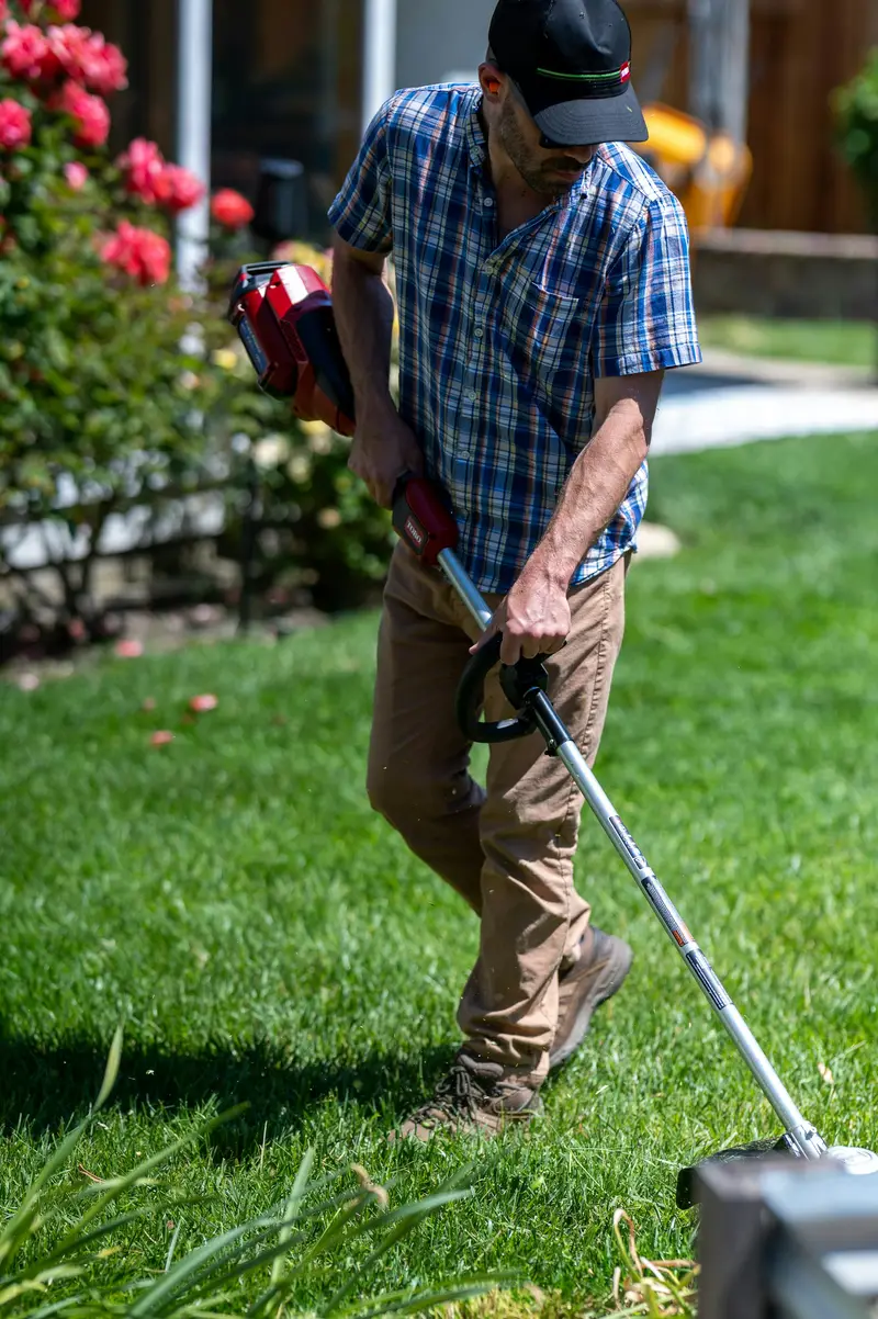 A lawn care worker edging along a flower bed with a string trimmer